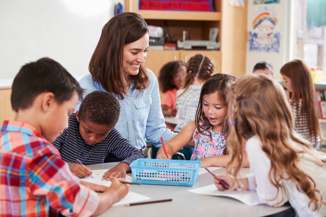 Teacher sitting at table with young school kids