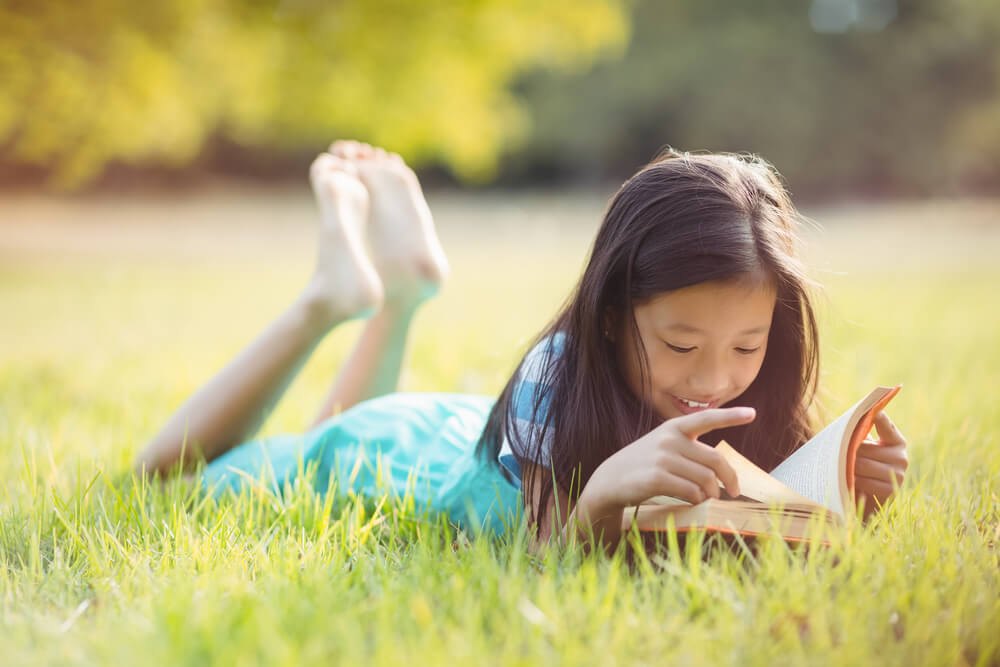 Young Girl Reads in the Grass Over the Summer School Break