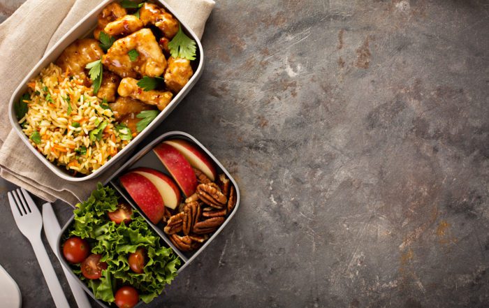 examples of lunchboxes, one is orange chicken with rice and the other is apple slices, walnuts and a salad