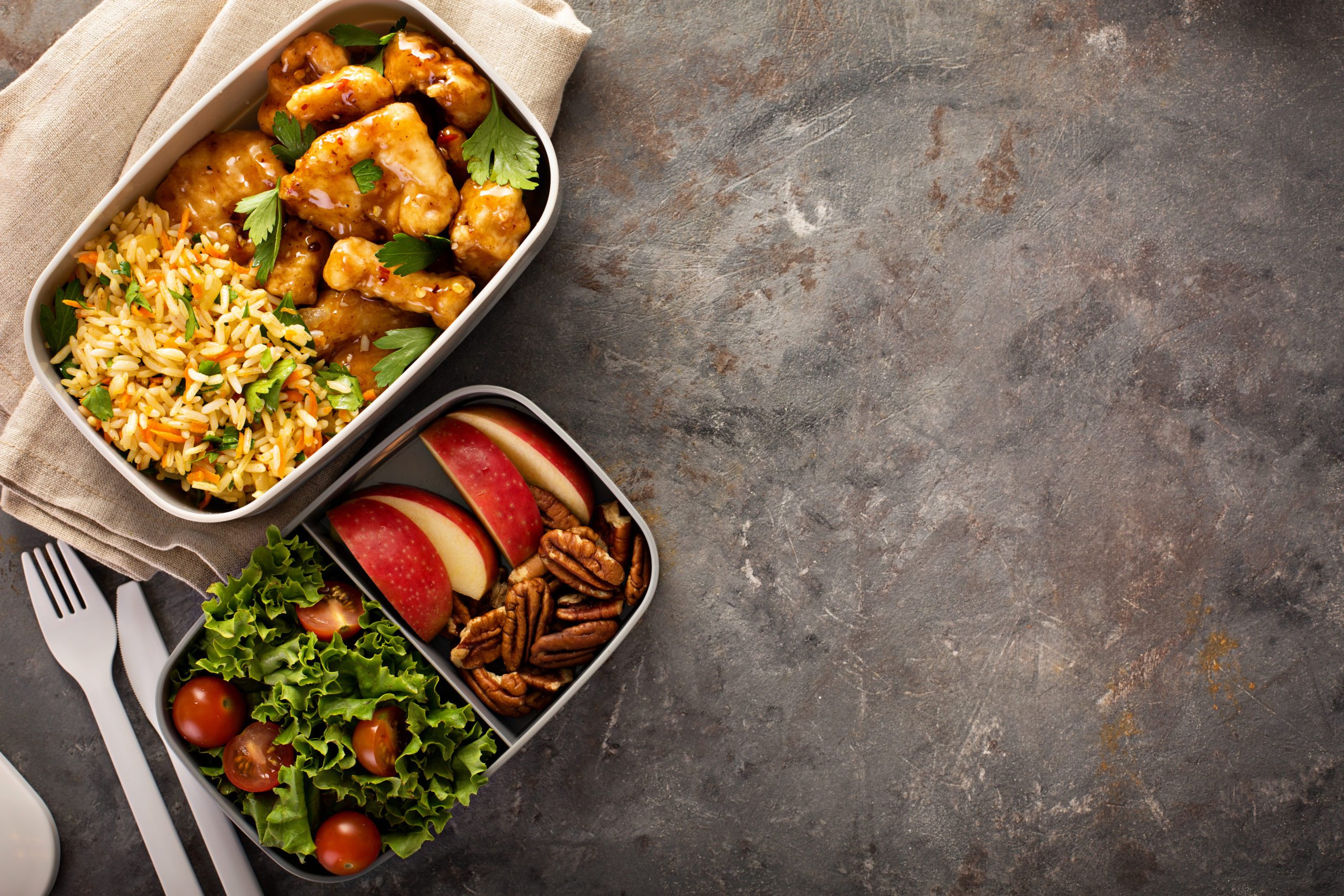 examples of lunchboxes, one is orange chicken with rice and the other is apple slices, walnuts and a salad